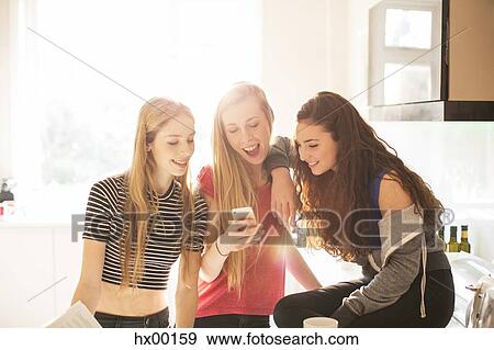 Stock Photo - Teenage girls texting with cell phone in sunny kitchen. Fotosearch