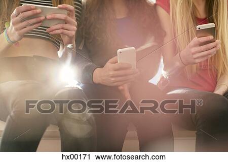 Stock Image - Teenage girls texting with cell phones in a row. Fotosearch
