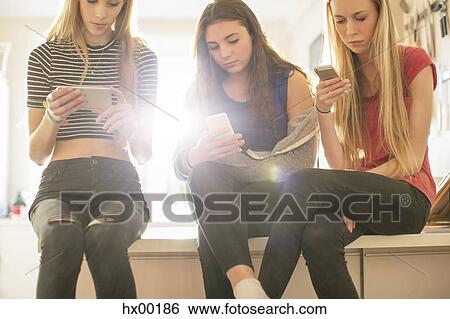 Stock Photograph - Teenage girls texting with cell phones in kitchen. Fotosearch