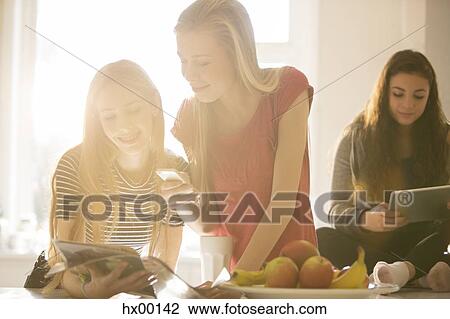 Stock Image - Teenage girls using cell phone and digital tablets. Fotosearch