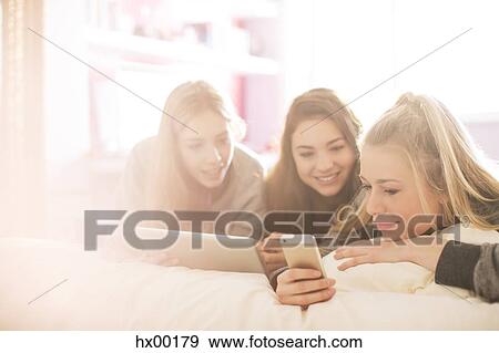Teenage girls using cell phone and digital tablet in sunny bedroom View Large Photo Image Stock Photo - Teenage girls using cell phone and digital tablet in sunny bedroom. Fotosearch