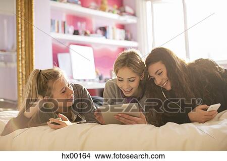 Picture - Teenage girls using cell phones and digital tablet on bed. Fotosearch