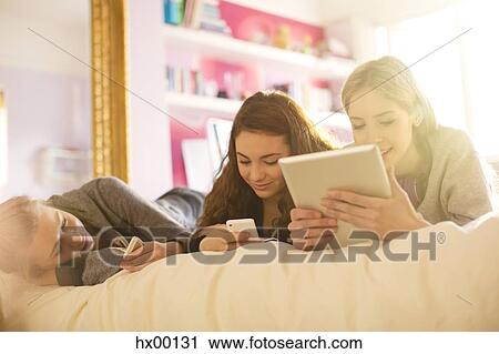 Teenage girls using cell phones and digital tablet on bed View Large Photo Image Stock Image - Teenage girls using cell phones and digital tablet on bed. Fotosearch