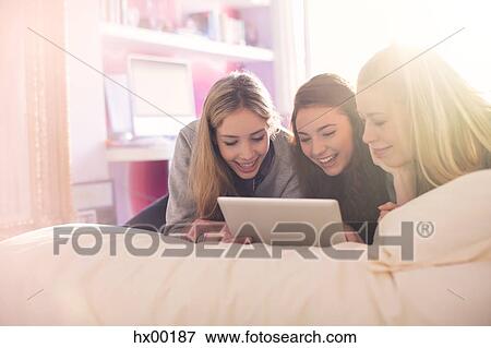 Teenage girls using digital tablet on bed in sunny bedroom View Large Photo Image Stock Photo - Teenage girls using digital tablet on bed in sunny bedroom. Fotosearch