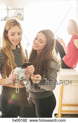Stock Image - Teenage girls using instant camera. Fotosearch