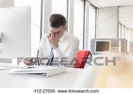 Stock Photography - Tired businessman rubbing eyes at computer in office. Fotosearch