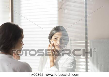 Woman applying moisturizer to cheek in bathroom mirror View Large Photo Image Stock Image - Woman applying moisturizer to cheek in bathroom mirror. Fotosearch
