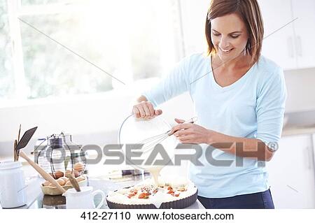 Stock Image - Woman cooking tomato quiche in kitchen. Fotosearch