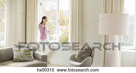 Woman drinking coffee and talking on cell phone at living room window View Large Photo Image Stock Photography - Woman drinking coffee and talking on cell phone at living room window. Fotosearch