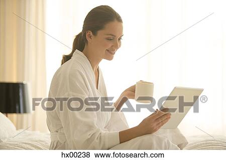Woman in bathrobe drinking coffee and using digital tablet in bedroom View Large Photo Image Stock Photo - Woman in bathrobe drinking coffee and using digital tablet in bedroom. Fotosearch