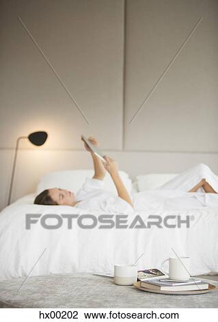 Woman in bathrobe laying on bed using digital tablet View Large Photo Image Stock Image - Woman in bathrobe laying on bed using digital tablet. Fotosearch