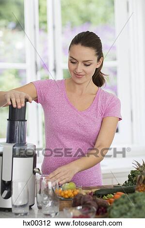 Stock Image - Woman juicing fresh fruits and vegetables. Fotosearch