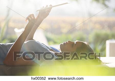 Stock Image - Woman laying and using digital tablet on patio. Fotosearch