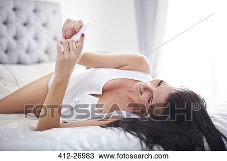 Woman laying on bed texting with cell phone View Large Photo Image Stock Image - Woman laying on bed texting with cell phone. Fotosearch