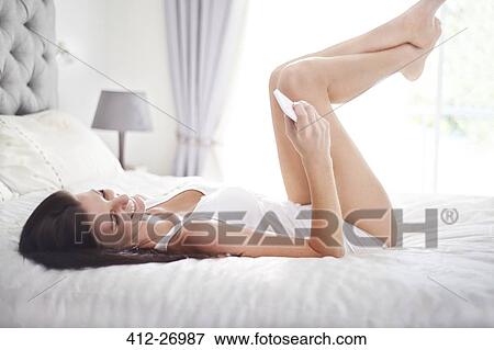 Stock Photo - Woman laying on bed texting with cell phone. Fotosearch