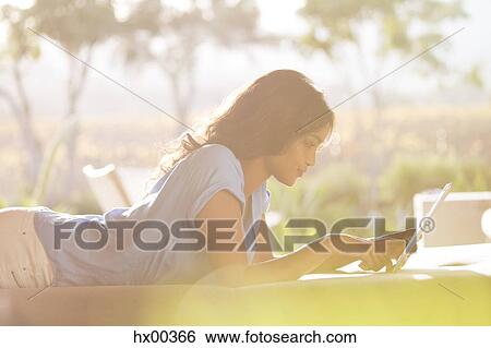 Woman laying using digital tablet on sunny patio View Large Photo Image Stock Photograph - Woman laying using digital tablet on sunny patio. Fotosearch
