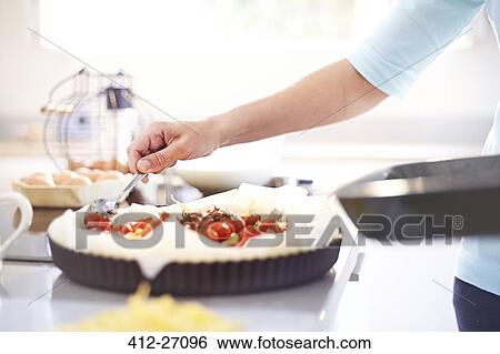 Stock Photograph - Woman preparing tomato quiche in kitchen. Fotosearch