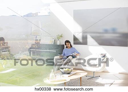 Stock Photo - Woman reading magazine in sunny living room. Fotosearch