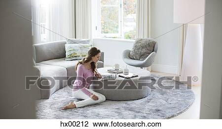 Woman reading magazine on ottoman in living room View Large Photo Image Stock Image - Woman reading magazine on ottoman in living room. Fotosearch