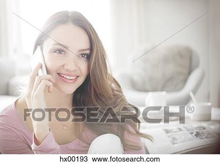 Stock Image - Woman talking on cell phone in living room. Fotosearch