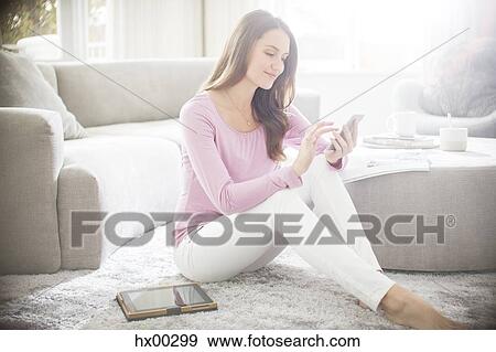 Stock Photo - Woman texting on cell phone in living room. Fotosearch