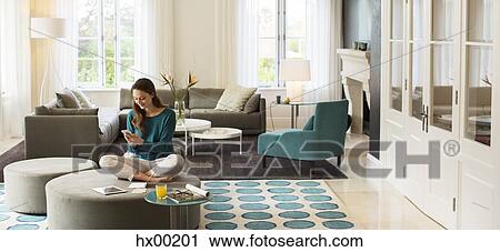 Woman texting on cell phone on ottoman in living room View Large Photo Image Stock Image - Woman texting on cell phone on ottoman in living room. Fotosearch