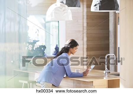 Picture - Woman using digital tablet in kitchen. Fotosearch