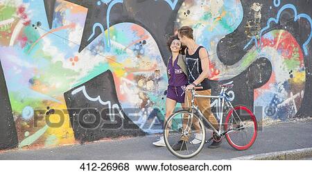 Young couple with bicycle hugging and walking along urban multicolor graffiti wall View Large Photo Image Stock Photo - Young couple with bicycle hugging and walking along urban multicolor graffiti wall. Fotosearch