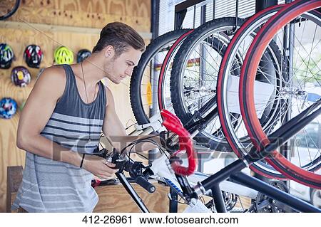 Stock Image - Young man examining bicycle on rack in bicycle shop. Fotosearch