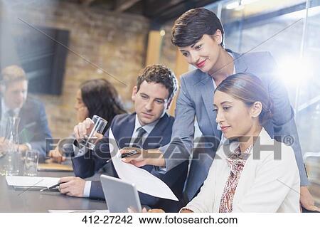 Stock Image - Business people with paperwork and digital tablet in conference room. Fotosearch