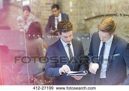 Businessmen discussing paperwork outside conference room meeting View Large Photo Image Stock Photo - Businessmen discussing paperwork outside conference room meeting. Fotosearch