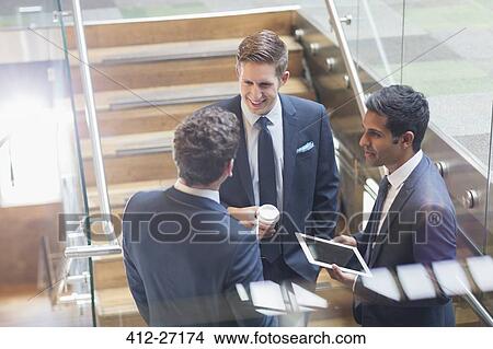 Picture - Businessmen with digital tablet and coffee talking on stairs. Fotosearch