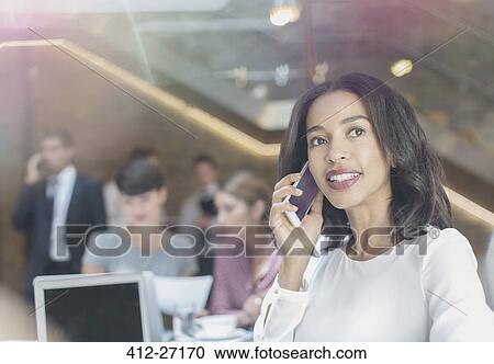 Stock Image - Businesswoman talking on cell phone in office. Fotosearch