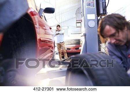 Stock Image - Customer talking on cell phone and checking the time in auto repair shop. Fotosearch