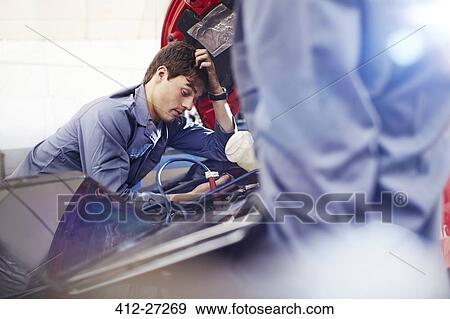 Stock Photo - Frustrated mechanic looking down at engine in auto repair shop. Fotosearch