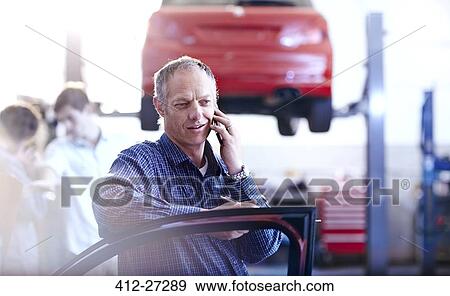 Stock Photo - Man talking on cell phone in auto repair shop. Fotosearch