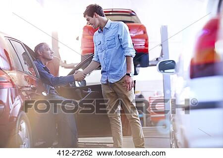 Stock Image - Mechanic and customer handshaking in auto repair shop. Fotosearch
