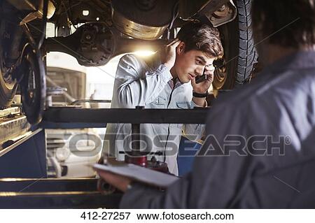 Mechanic and customer talking on cell phone under car View Large Photo Image Stock Photo - Mechanic and customer talking on cell phone under car. Fotosearch