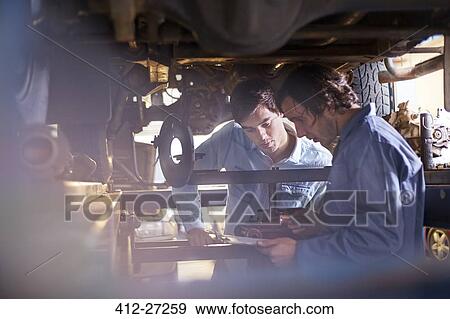 Mechanic and customer under car in auto repair shop View Large Photo Image Stock Photo - Mechanic and customer under car in auto repair shop. Fotosearch