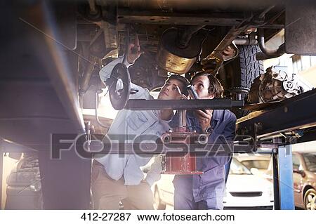 Stock Photo - Mechanic and customer under car in auto repair shop. Fotosearch