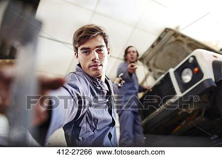 Stock Photograph - Mechanic reaching for tool below car in auto repair shop. Fotosearch