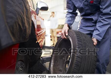 Stock Image - Mechanic replacing tire in auto repair shop. Fotosearch