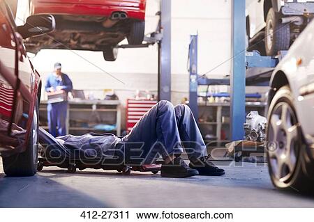 Stock Image - Mechanic under car in auto repair shop. Fotosearch