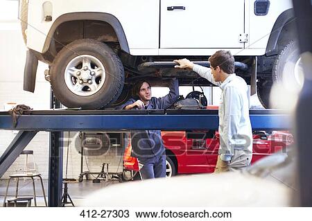 Mechanic under car talking to customer in auto repair shop View Large Photo Image Stock Image - Mechanic under car talking to customer in auto repair shop. Fotosearch