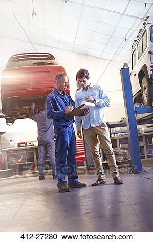 Mechanic with clipboard talking to customer in auto repair shop View Large Photo Image Stock Image - Mechanic with clipboard talking to customer in auto repair shop. Fotosearch