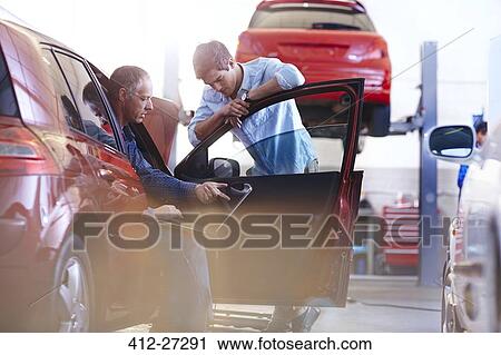Stock Image - Mechanic with laptop talking to customer at car in auto repair shop. Fotosearch
