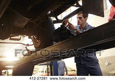 Stock Image - Mechanic working under car in auto repair shop. Fotosearch