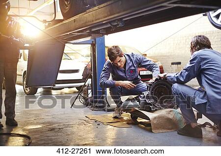 Stock Image - Mechanics examining part in auto repair shop. Fotosearch