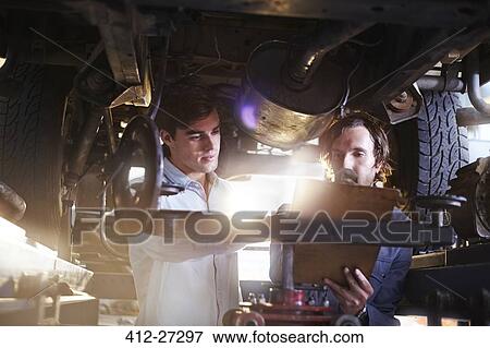 Stock Photo - Mechanics with clipboard under car in auto repair shop. Fotosearch