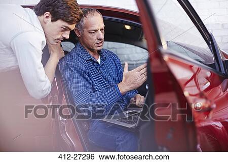 Stock Photograph - Mechanics with laptop at car in auto repair shop. Fotosearch